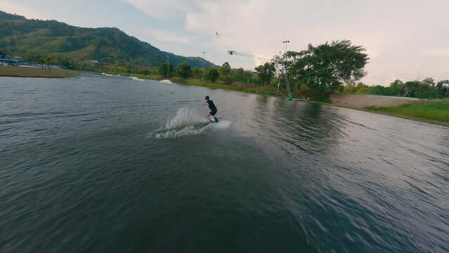 Aerial view sport man riding wakeboarding flat and jibbing tricks slides tropical sunny seascape. FPV sport drone follow shot active extreme male enjoy speed splash ride wakeboard cable jump surf 4k
