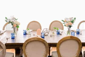 A beautiful decorated dining table with round, oval chairs and a simple centerpiece with flower...
