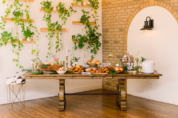 A beautiful decorated breakfast buffet table with food, and green plants are hanging on the wall 