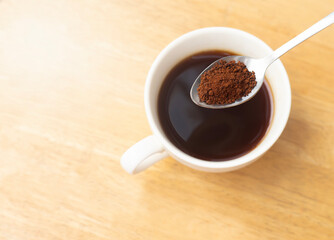 An image close-up top view or flat lay ground black coffee instant roasted on the spoon is a hot drink for beverage morning is a wood table background with copy space for text.