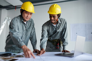 Diverse team of civil engineers discussing details of construction plan on table