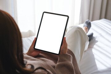 Mockup image of a woman holding digital tablet with blank desktop white screen while laying on a bed - Powered by Adobe