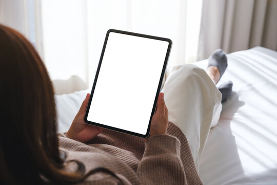 Mockup image of a woman holding digital tablet with blank desktop white screen while laying on a bed