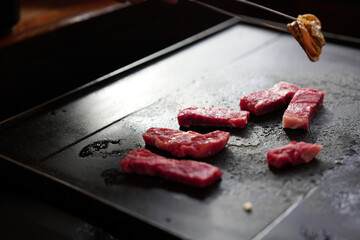 Japanese premium beef sliced with juicy marbled line grilling on black barbecue plate while hand pick mussel seafood by chopsticks for eating lunch in Asian restaurant