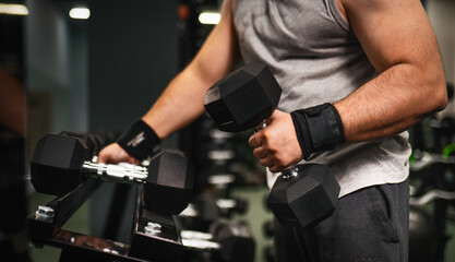 A swarthy man with a beard is holding huge dumbbells in his hands and preparing to perform a biceps...