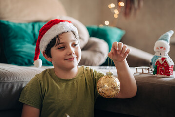 Naklejka premium Kid boy decorating Christmas tree put off balls from the box authentic real celebration image lifestyle. Xmas with family children fun at cozy home