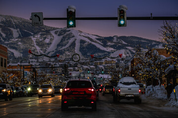 View of main street in Colorado resort town decorated for charismas at night in winter; mountain with ski runs in background - obrazy, fototapety, plakaty