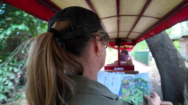 Women riding on a sightseeing adventure train reading a map while traveling through a tropical location.