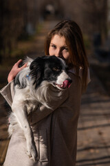 Caucasian woman holding a border collie in her arms while walking in the autumn park. Portrait of a girl with a dog.