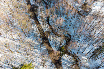 Aerial photo of a country road going through a winter forest next to a stream in a ravine