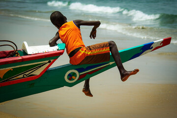 Enfant assit sur une pirogue de pêche au Sénégal - obrazy, fototapety, plakaty