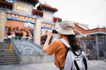 Deurstickers Back view of tourist women blogger or Influencer are Taking photo while traveling in Hong Kong with the blur background of a most popular Chinese temple in travel and solo travel concept. © boophuket