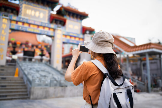 Back view of tourist women blogger or Influencer are Taking photo while traveling in Hong Kong with the blur background of a most popular Chinese temple in travel and solo travel concept.