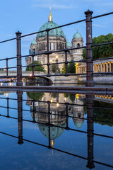 The Berlin Cathedral and the river Spree at dusk with handrails and a reflection in a puddle