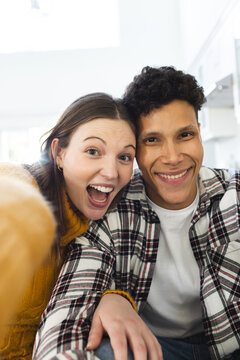Portrait of happy diverse couple sitting on couch and embracing at home, copy space