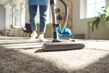 Housewife using vacuum cleaner on rug during clean-up at home. Crop shot of young woman vacuuming...