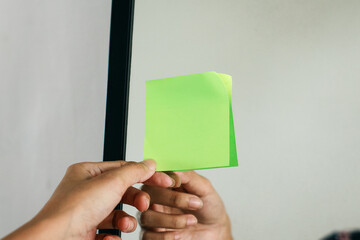 Hand putting blank green sticky notes in the mirror