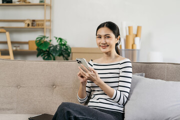 Women conduct financial transactions via smartphone sitting on sofa.