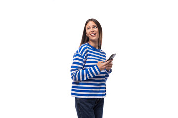 young confident european brunette woman dressed in striped blue clothes holding a smartphone in her hand