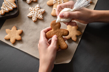 Christmas gingerbread cookie decoration. Hands holding gingerbread man cookie and piping bag with icing, making cookie decor. Winter holiday traditional family cooking. Selective focus, lifestyle