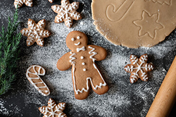 Traditional gingerbread cookie family baking at home. Gingerbread man, snowflake and cane shape cookies, rolled dough, fir branch on black table background with flour. Soft selective focus, lifestyle