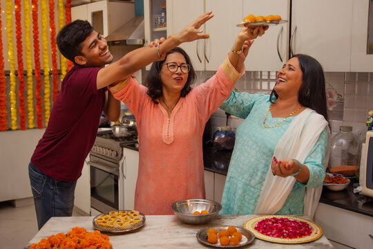 Young boy trying to steal laddoo while his mother and grandmother making those laddoos in the kitchen on the occasion of Diwali