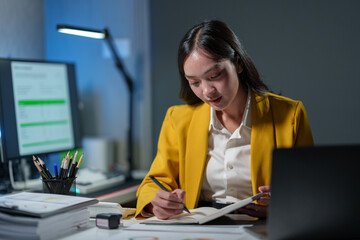 Asian businesswoman writes Take notes on startup business planning ideas. Financial Marketing, organizational management guidelines on a laptop in the office. - obrazy, fototapety, plakaty
