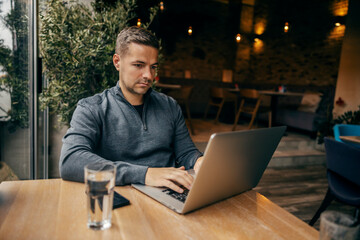 A serious virtual assistant is sitting in cafe and using his laptop.