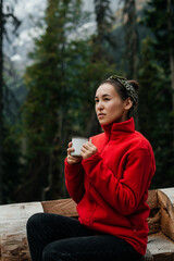 a thoughtful girl with a cup of coffee in the mountains and autumn forest