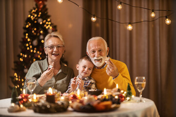 Grandparents and grandchild showing gingerbread cookies at the camera while sitting at home on...