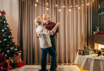 A happy senior couple is dancing on christmas and new year's eve at cozy apartment.