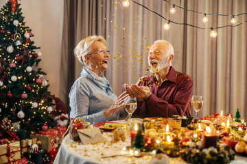 A festive christmas senior couple is celebrating christmas and new year's eve with confetti at home...