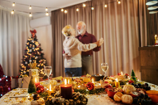 Selective focus on christmas table with ornaments and food with blurry senior couple dancing on christmas and new year's eve..