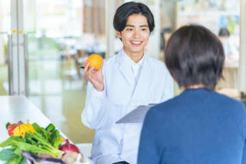 女性に野菜や果物を勧める若い白衣の男性　管理栄養士