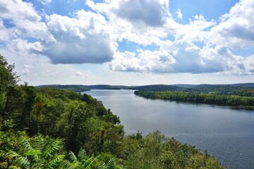 Beautiful scenic summer view along the Connecticut River with dense green foliage on either side and fluffy white clouds in blue sky overhead