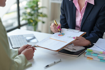 Two Asian businesswomen talk, consult, discuss work with presentation of project ideas, growth analysis, marketing and investment plans, data from charts in organization in office.