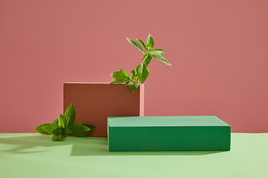 Blank minimalist empty showcase template. Red and green rectangular podiums decorated with spearmint leaves on pink and green background. Space to place your product. Front view