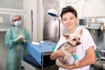 Boy visitors veterinary clinic, happy teenage guy holding Yorkshire terrier in his hands, are...