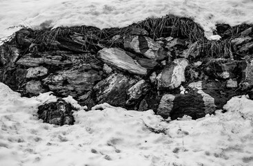 black and white stone surrounded by snow in the mountains. large stones in the middle of the snow. rocks of mountain in winter. snow covered rocky hill. black and white winter rocky landscape