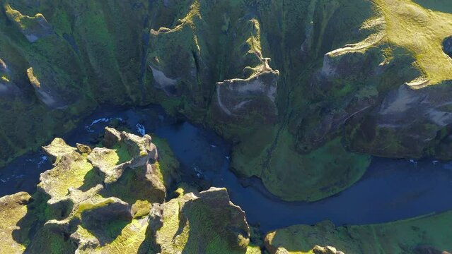 Breathtaking aeral view of steep stone walls of ancient rock formations generously covered with green moss and winding narrow river on a sunny day. High quality 4k footage