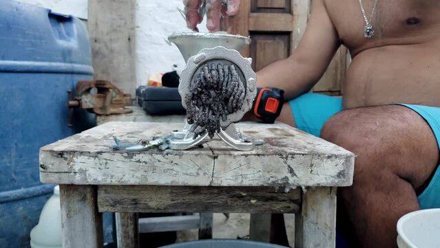 Hands man grinds small fishes bait to chum use drill to speed up manual work