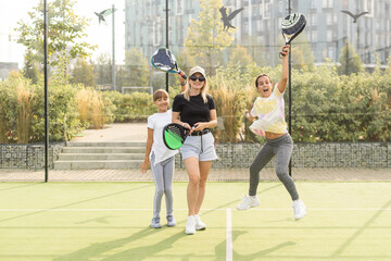 Obraz premium Young sporty woman with children playing padel game in court on sunny day