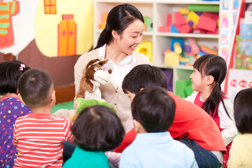 Female teacher playing hand puppet game with cute kindergarten children