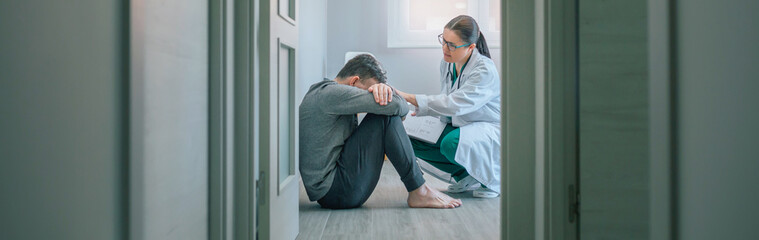 Female doctor reassuring and helping with empathy to male patient sitting on the room floor of a...