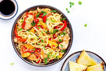 Stir fry egg noodles with chicken slices, pineapple, red paprika, chives, soy sauce and sesame seeds in ceramic bowl. Asian cuisine dish. White table background, top view