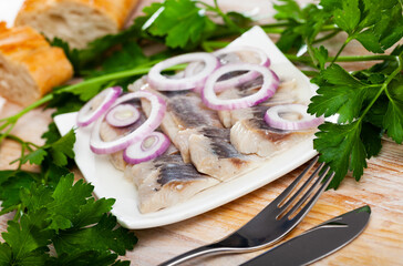Plate with slices of salted fillet of herring with onion on wooden table with fresh parsley