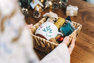 Woman s hands wrapping Christmas eco gift wicker basket, close up. Unprepared presents on wooden...