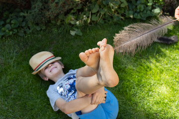 joyful child lies on the lawn, his bare feet tickled by a large ostrich feather. Fun family time...