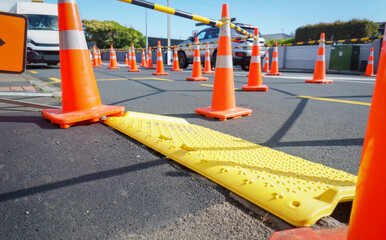 Yellow road safety trench cover and orange traffic cones on the street. Cars driving on the...