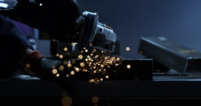 Super slow motion close up of blacksmith welder is smoothing metal steel with industrial angle grinder with flying sparks in workshop.